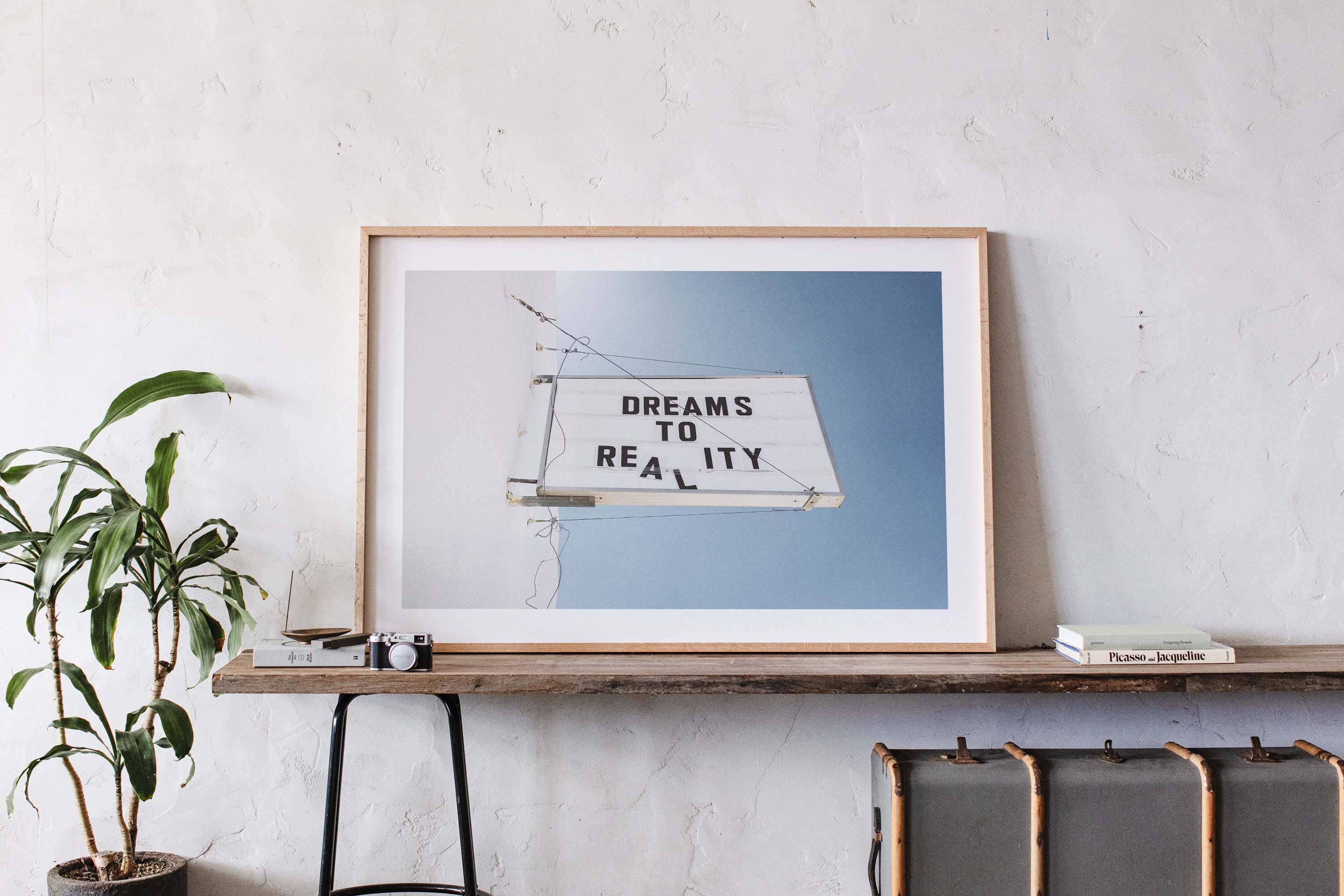 Minimal photo print of a marquee sign on a white wall reading “DREAMS TO REALITY” against a clear blue sky.