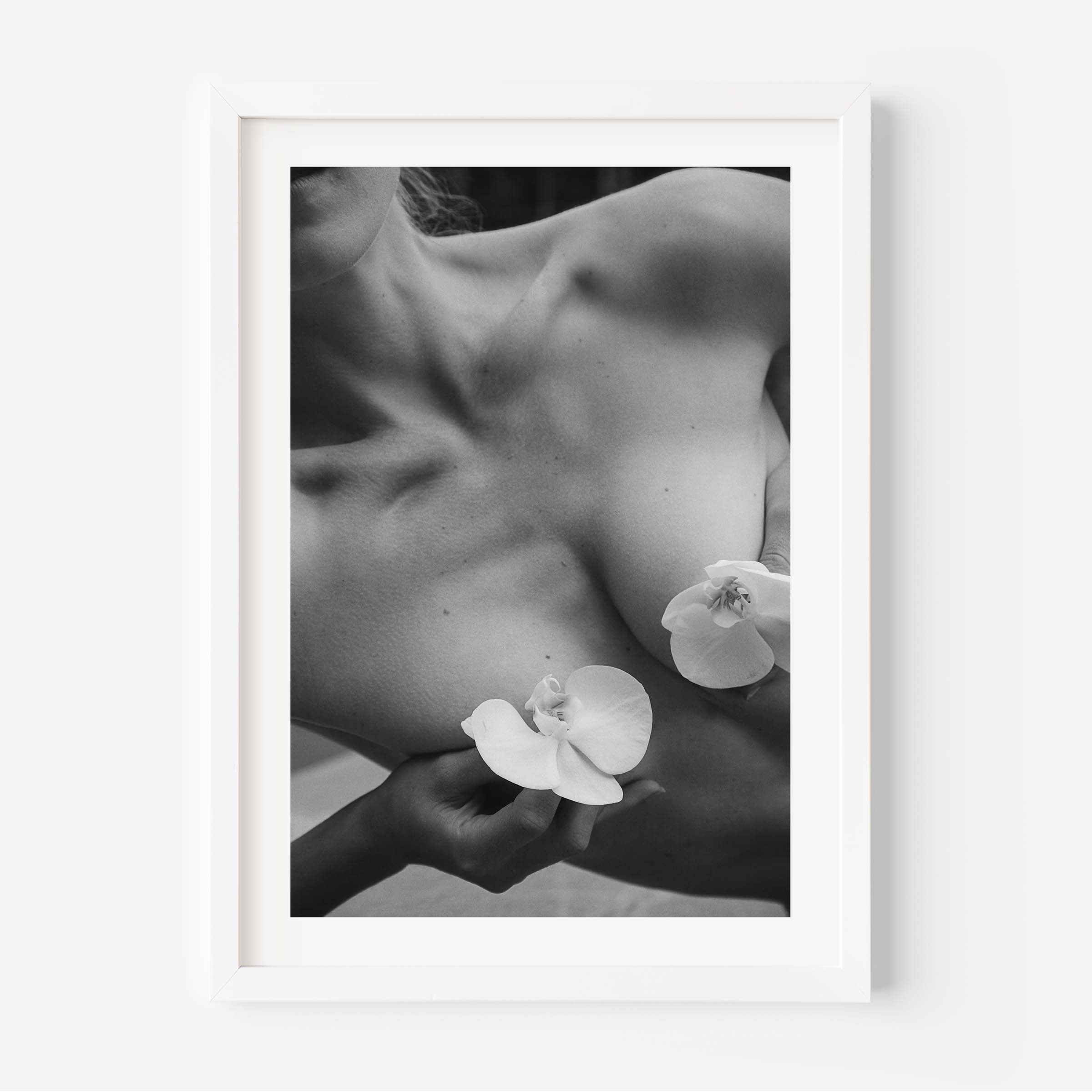 Framed black-and-white photograph of a woman’s collarbone with white orchid flowers, styled in a Parisian interior with molding, mirror, and chair — by Britt Van der Meijden.